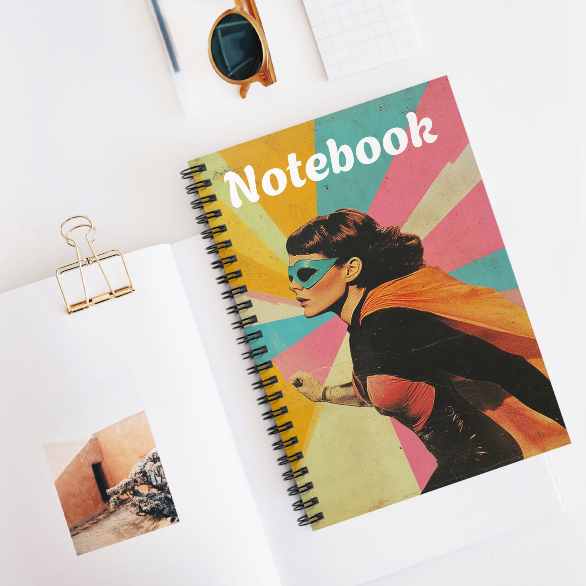 The image features a spiral notebook with a vibrant Golden Age-inspired superheroin on the cover. The ruled lines and durable spiral binding are visible, making it an ideal companion for note-taking, journaling, and creative writing.